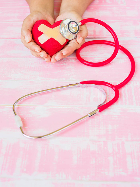 Health and medical, love and valentine concept. Red heart on a woman hand with red stethoscope on the pink wood background - Photo, Image