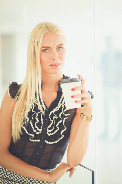 Businesswoman holding a cup of coffee standing in office . - Photo, Image
