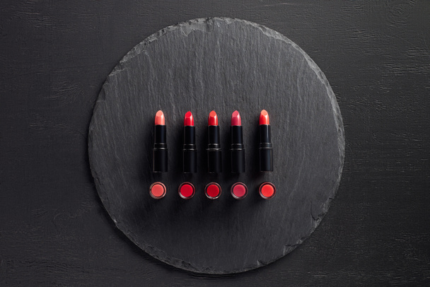 Row of red lipsticks on round slate background - Foto, Imagem