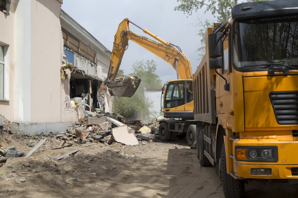 Excavator on wheels do the loading of construction debris and debris of the walls of the old building after the destruction, in the body of a dump truck - Photo, Image