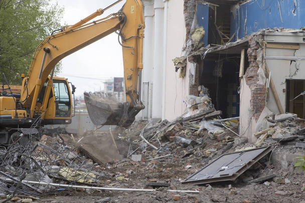 De vernieling van de muren van het oude gebouw en het opruimen van bouwafval met een emmer van een graafmachine. - Foto, afbeelding