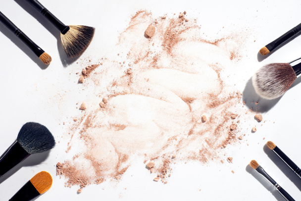 Quadro de pincéis de maquiagem no fundo branco com pó de rosto espalhado
 - Foto, Imagem