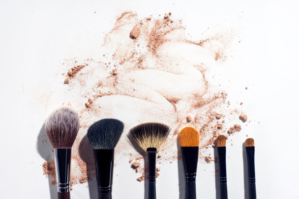 Set of brushes in a row on white background with scattered face powder - Photo, Image