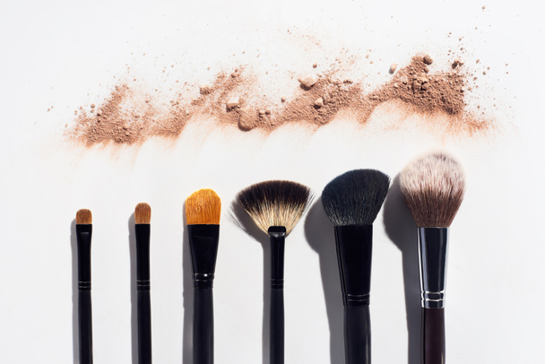 Line of scattered face powder and makeup brushes on white background - Photo, Image