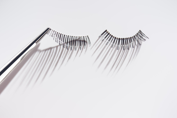Fixing fake eyelashes with tweezers on white background - Photo, Image