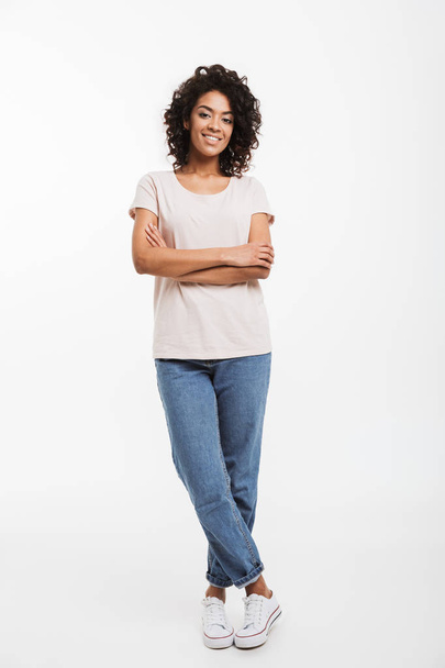 Full length portrait of beautiful american woman wearing jeans and t-shirt standing with arms folded and smile isolated over white background - Photo, image