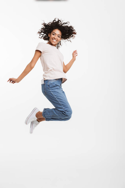 Full length portrait of satisfied american woman wearing jeans and t-shirt jumping and rejoicing with perfect smile isolated over white background - Foto, immagini