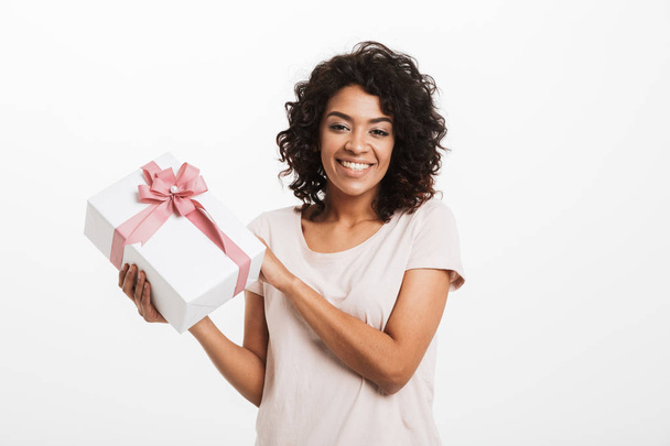 Portrait of a smiling young afro american woman holding present box isolated over white background - Фото, изображение