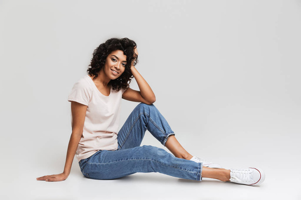 Portrait of happy young afro american woman resting while sitting on a floor isolated over white background - Zdjęcie, obraz