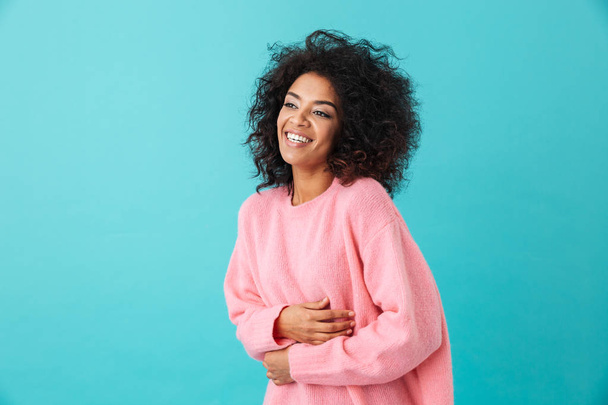 Multicolor image of pretty woman 20s with afro hairstyle laughing out loud and touching her belly isolated over blue background - Fotografie, Obrázek