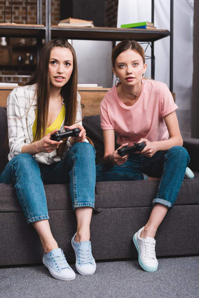 two female friends with joysticks in hands playing video game at home - Foto, immagini