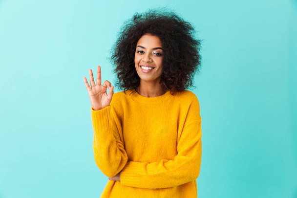 Content american woman in colorful shirt smiling on camera and gesturing ok sign isolated over blue background - Fotó, kép