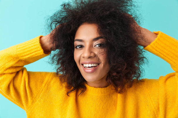 Colorful portrait closeup of curly woman in yellow shirt looking on camera while holding hands behind her head isolated over blue background - Φωτογραφία, εικόνα