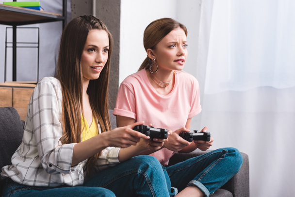 two focused female friends with joysticks in hands playing video game at home - Fotografie, Obrázek