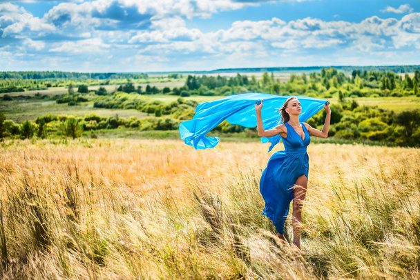 Muotokuva romanttinen hoikka nainen kävely vehnäpellolla, hänellä on yllään kirkkaan sininen tyylikäs mekko
  - Valokuva, kuva