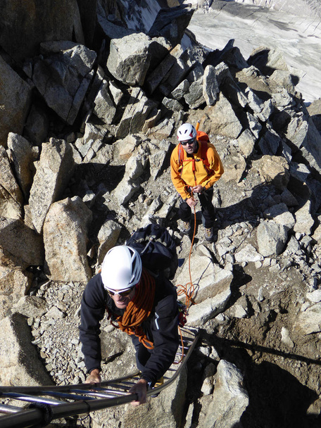 guida alpina e cliente si preparano a salire una scala fino all'uscita del loro percorso di arrampicata a Chamonix vicino al Monte Bianco
 - Foto, immagini