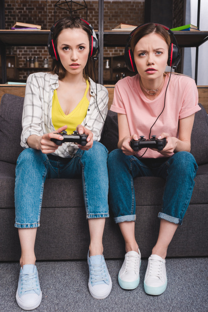 concentrado amigos do sexo feminino em fones de ouvido com joysticks em mãos jogando videogame
  - Foto, Imagem