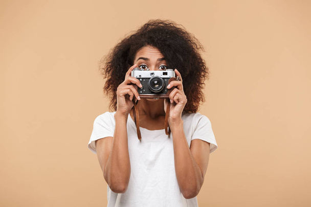 Portrait of a pretty young african woman taking photo with photo camera isolated over beige background - Fotografie, Obrázek