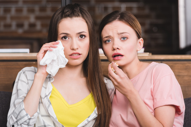 young woman wiping tears by napkin while her female friend eating popcorn and watching movie - Photo, Image