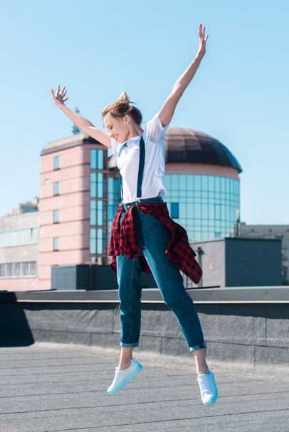 jonge lachende vrouw springen met brede armen op dak - Foto, afbeelding