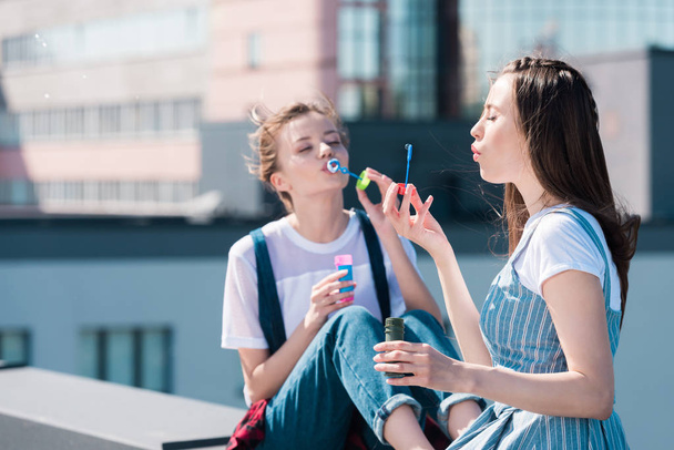 young attractive female friends using bubble blowers at rooftop - Фото, изображение