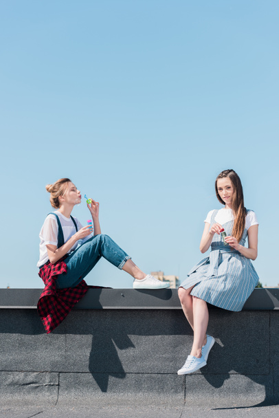 aantrekkelijke jonge vrouwelijke vrienden met behulp van bubble ventilatoren op dak  - Foto, afbeelding