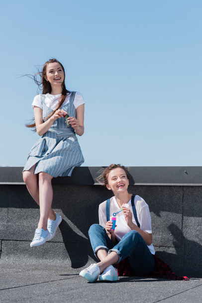 duas amigas sorridentes usando sopradores de bolhas no telhado
  - Foto, Imagem