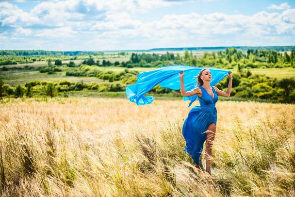 Retrato de mujer delgada romántica caminando en el campo de trigo, ella está usando vestido elegante azul brillante
  - Foto, imagen