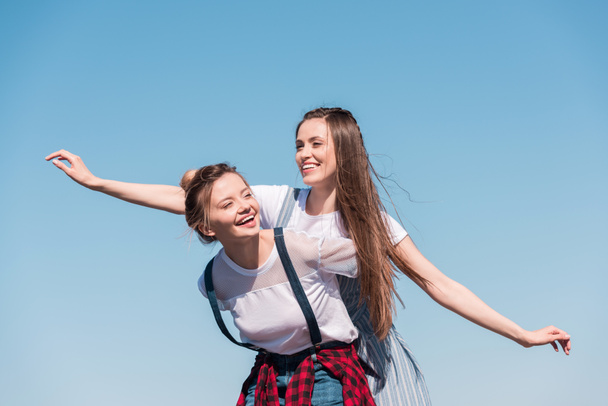 smiling young woman doing piggyback ride to female friend  - Fotoğraf, Görsel