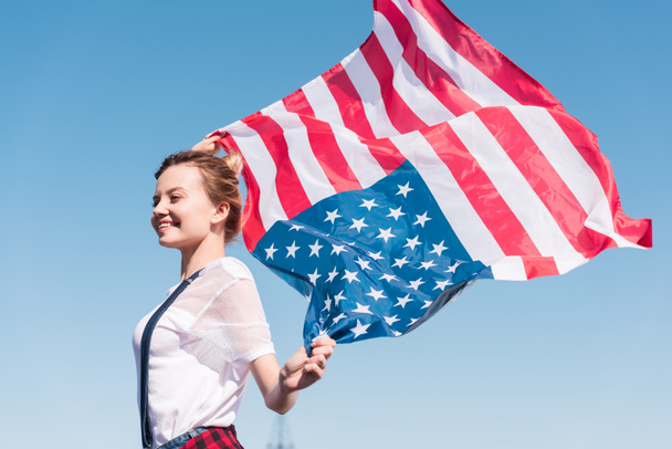 šťastná mladá žena drží vlajku Spojených států proti modré obloze, Den nezávislosti koncept - Fotografie, Obrázek