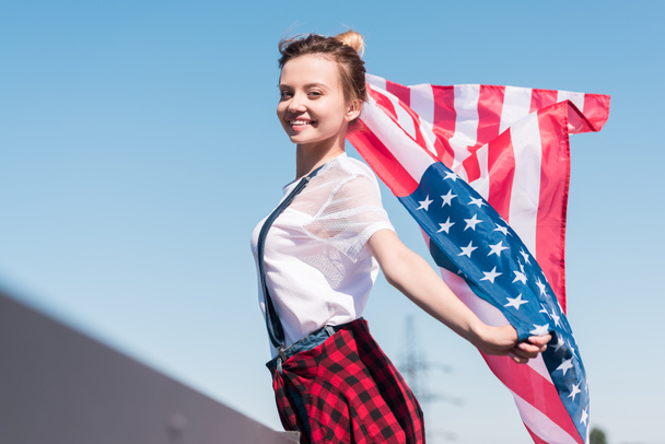smiling young woman holding american flag against blue sky, independence day concept - Φωτογραφία, εικόνα