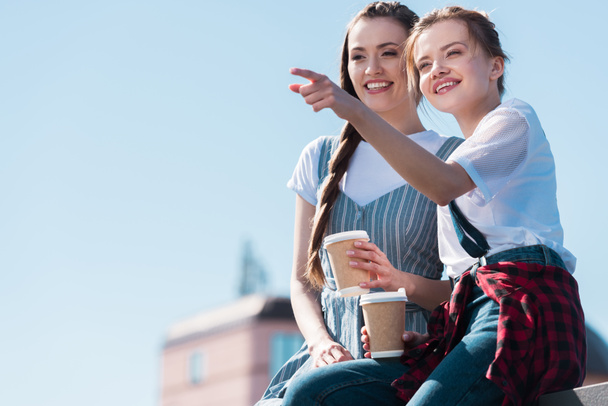 jeune femme pointant du doigt vers une amie souriante avec une tasse de café en papier
  - Photo, image