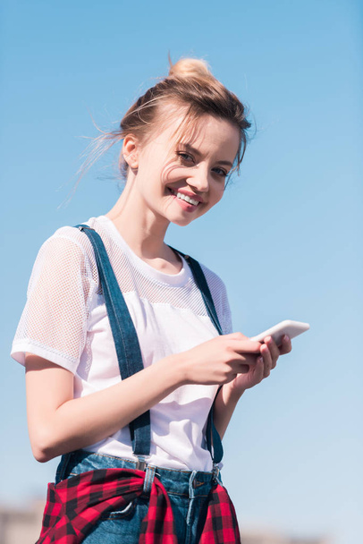 smiling young woman with smartphone against bright blue sky - Fotó, kép