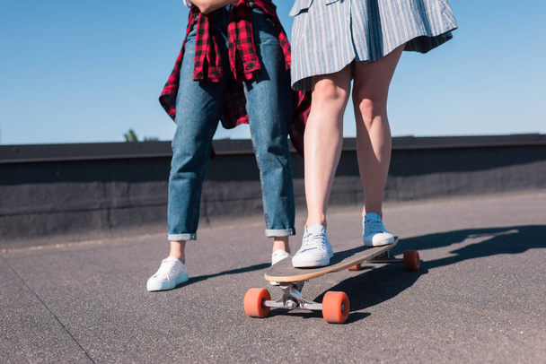 スケート ボードに乗って彼女の女友達を教える女性のショットをトリミング  - 写真・画像