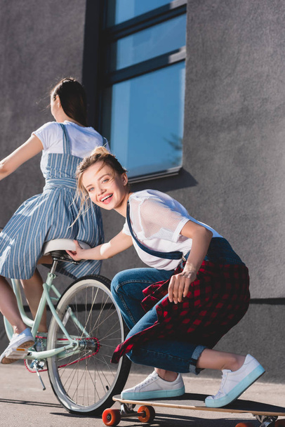 женщина ездит на велосипеде и буксирует свою улыбающуюся подругу на скейтборде
  - Фото, изображение