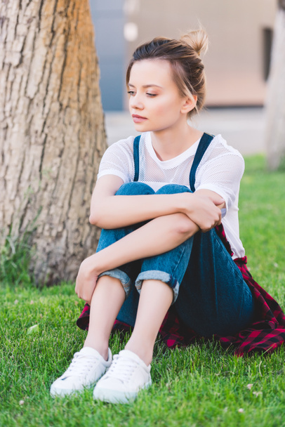 sad young woman sitting on green lawn in park - Fotó, kép