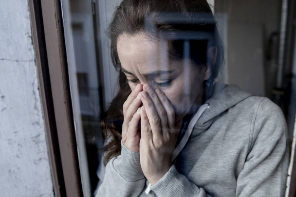 Close up of middle aged depressed latin woman standing at window and crying - Foto, imagen