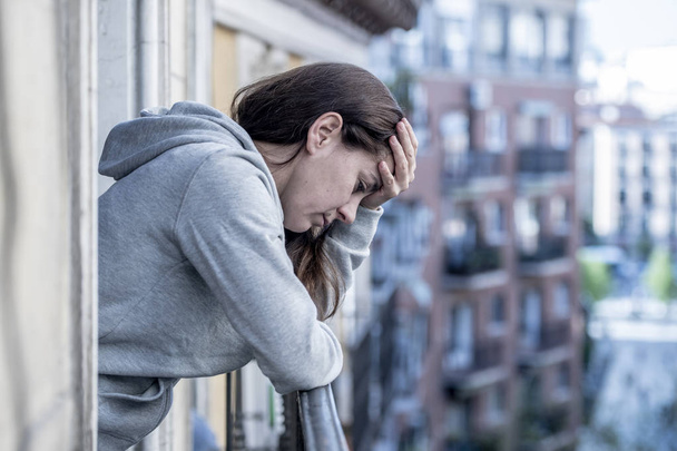 Depressed latin woman standing on balcony holding head with hand - Фото, зображення