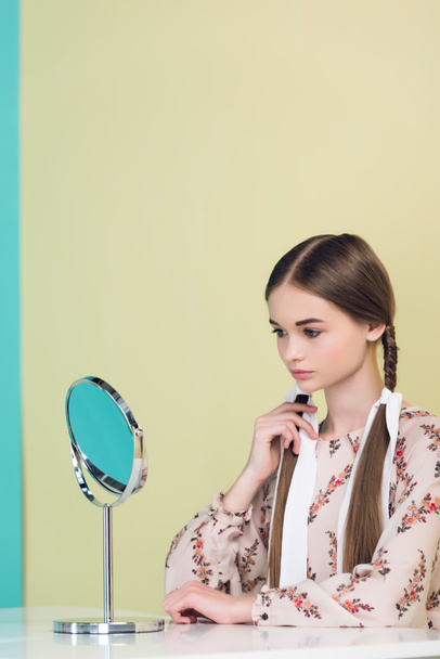 Teen κορίτσι κοιτάζοντας καθρέφτη και συγκινητικό της πλεξούδες, στο κίτρινο - Φωτογραφία, εικόνα