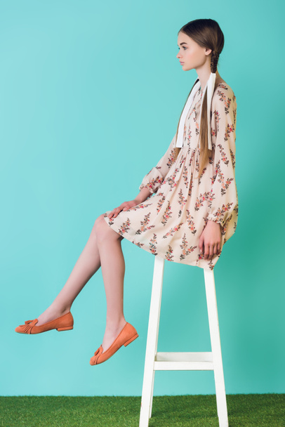 teen girl in summer dress with braids sitting on stool, on blue - Фото, изображение