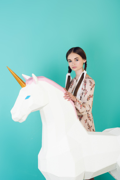 beautiful teen girl posing with big white unicorn isolated on turquoise - Foto, afbeelding