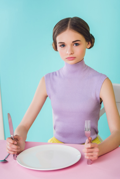 beautiful girl with knife, fork and empty plate sitting at table - Fotoğraf, Görsel