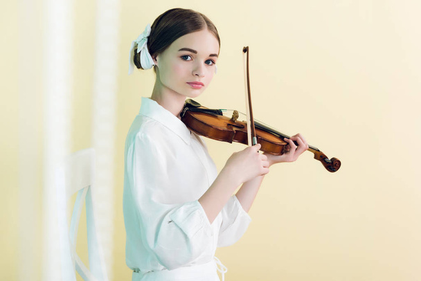 красивий підліток у білому вбранні грає на скрипці, ізольований на жовтому
 - Фото, зображення