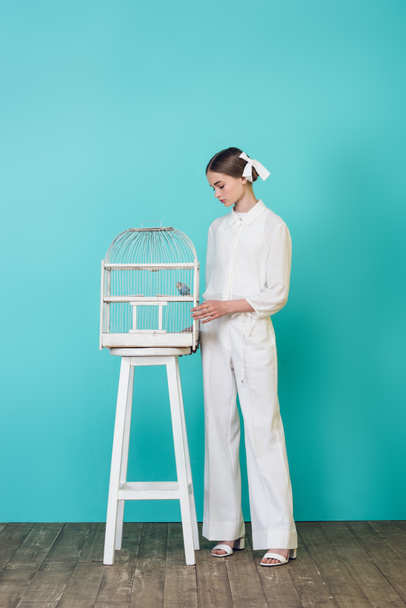 ragazza adolescente alla moda in elegante vestito bianco guardando pappagallo in gabbia, su turchese
 - Foto, immagini