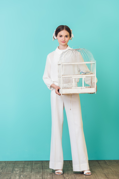 attractive fashionable girl holding parrot in cage, on turquoise - Photo, Image