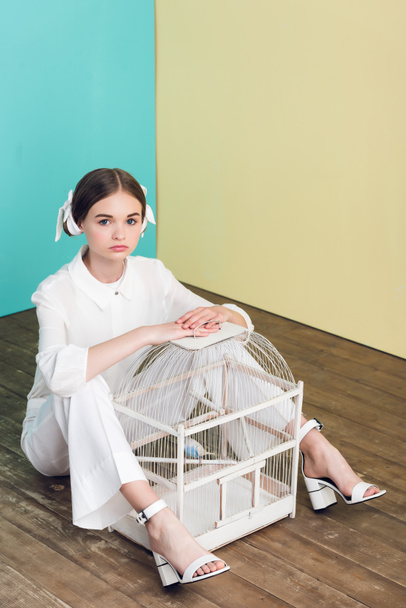 stylish teen girl with parrot in cage sitting on floor - Foto, Imagen