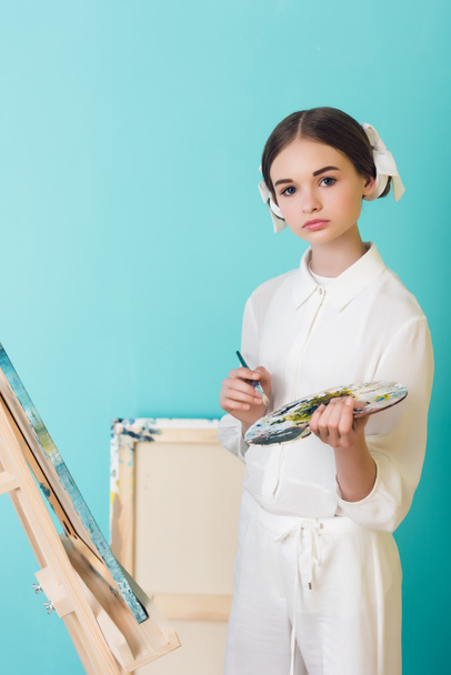 styling teen artist painting on easel with brush and palette, on turquoise - Photo, Image