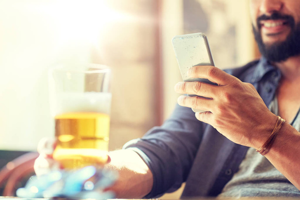 close up of man with smartphone and beer at pub - Foto, afbeelding