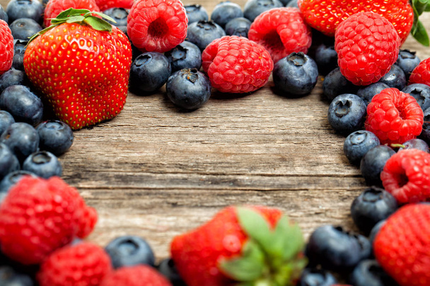Strawberry, raspberry and blueberries on wooden board background. Healthy eating, frame of assorted berries - Photo, Image