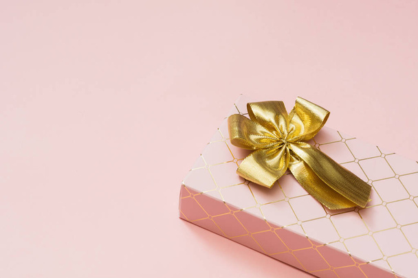 Female gift box with golden ribbon on punchy pastel pink. Birthday. Copy space. Top view. - Фото, изображение